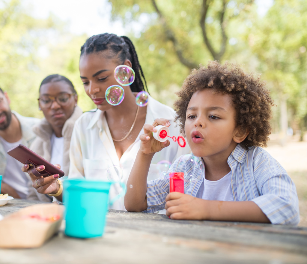 Mère distraite par son téléphone pendant que son fils joue avec des bulles de savon lors d'un pique-nique en famille