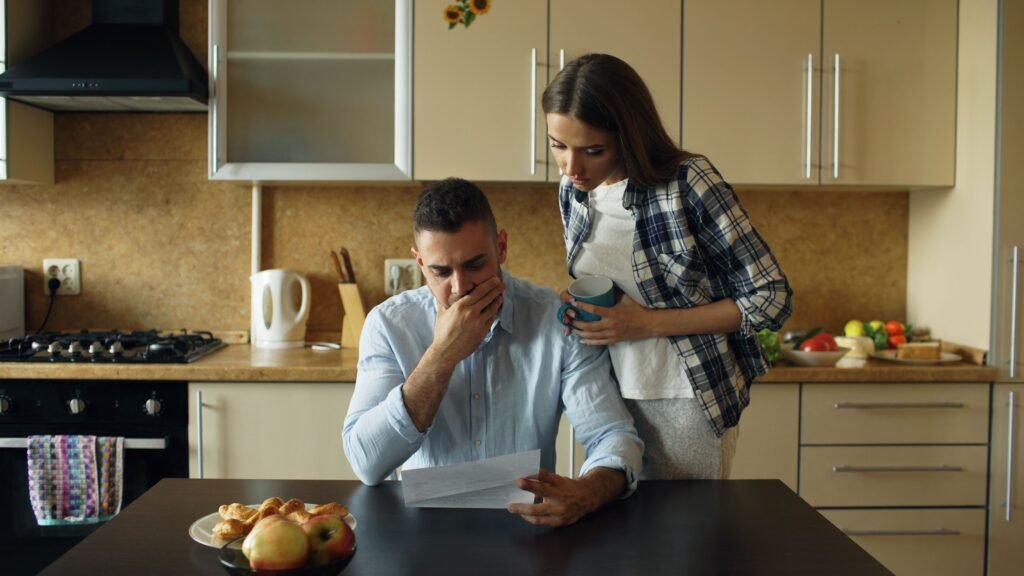 Couple looking surprised while reading their electricity bill at the kitchen table